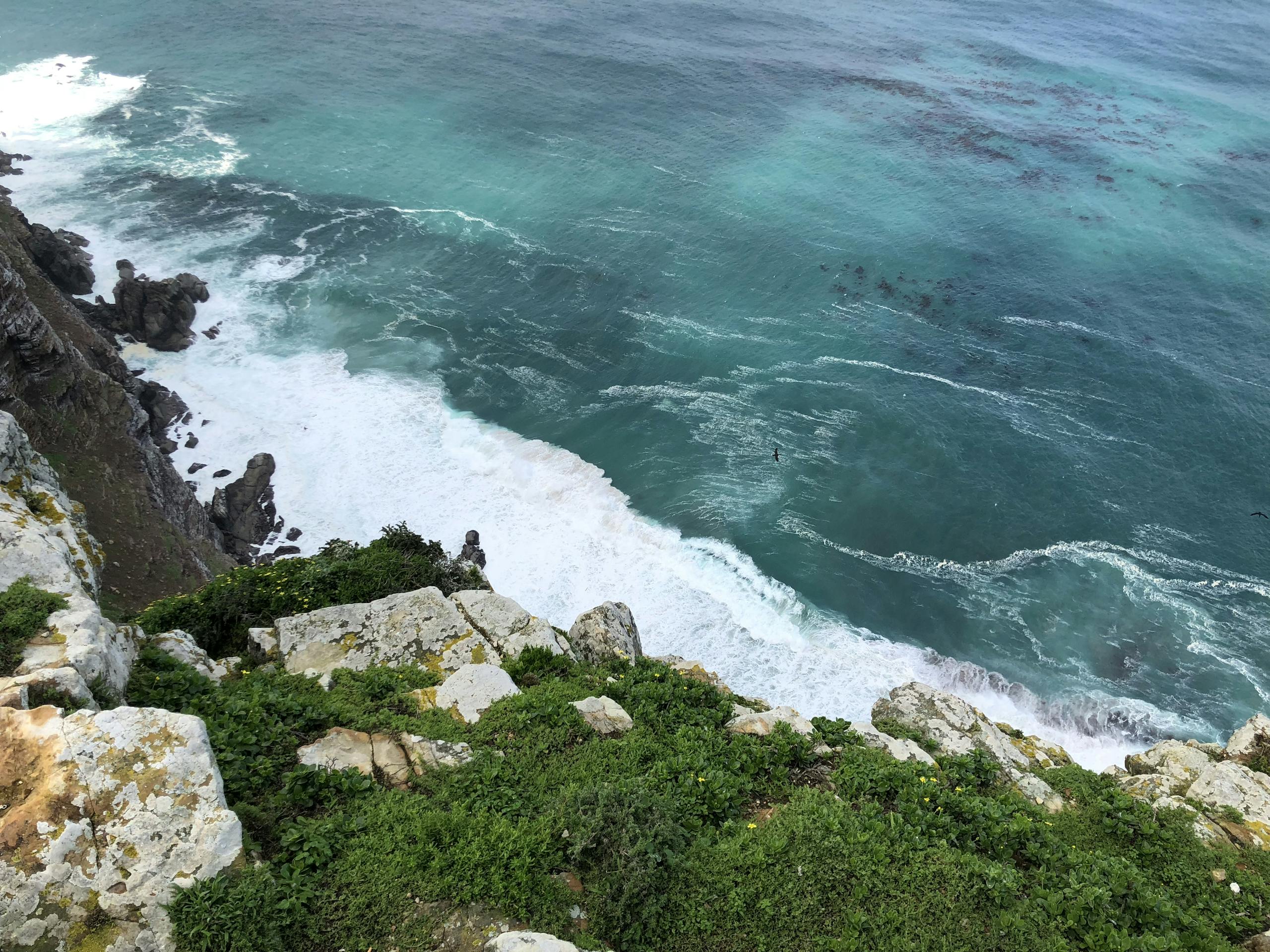 Dramatic aerial view of Cape Town's coastline with turquoise sea and rocky cliffs.